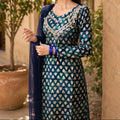 Woman wearing a traditional blue and green patterned dress with a matching dupatta, standing outdoors.