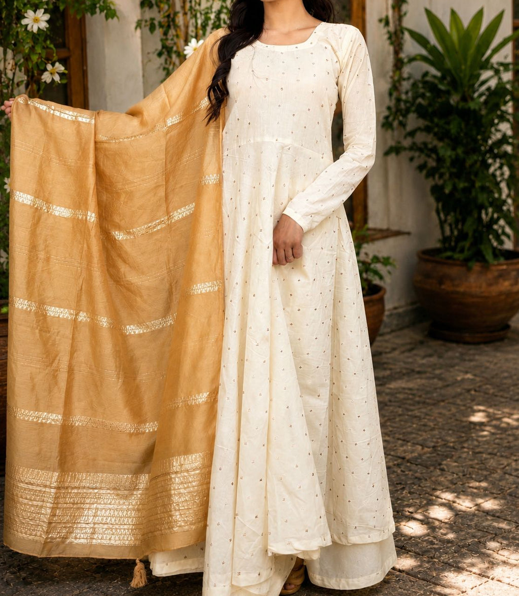 Woman wearing a white traditional outfit with a beige dupatta, standing outdoors.