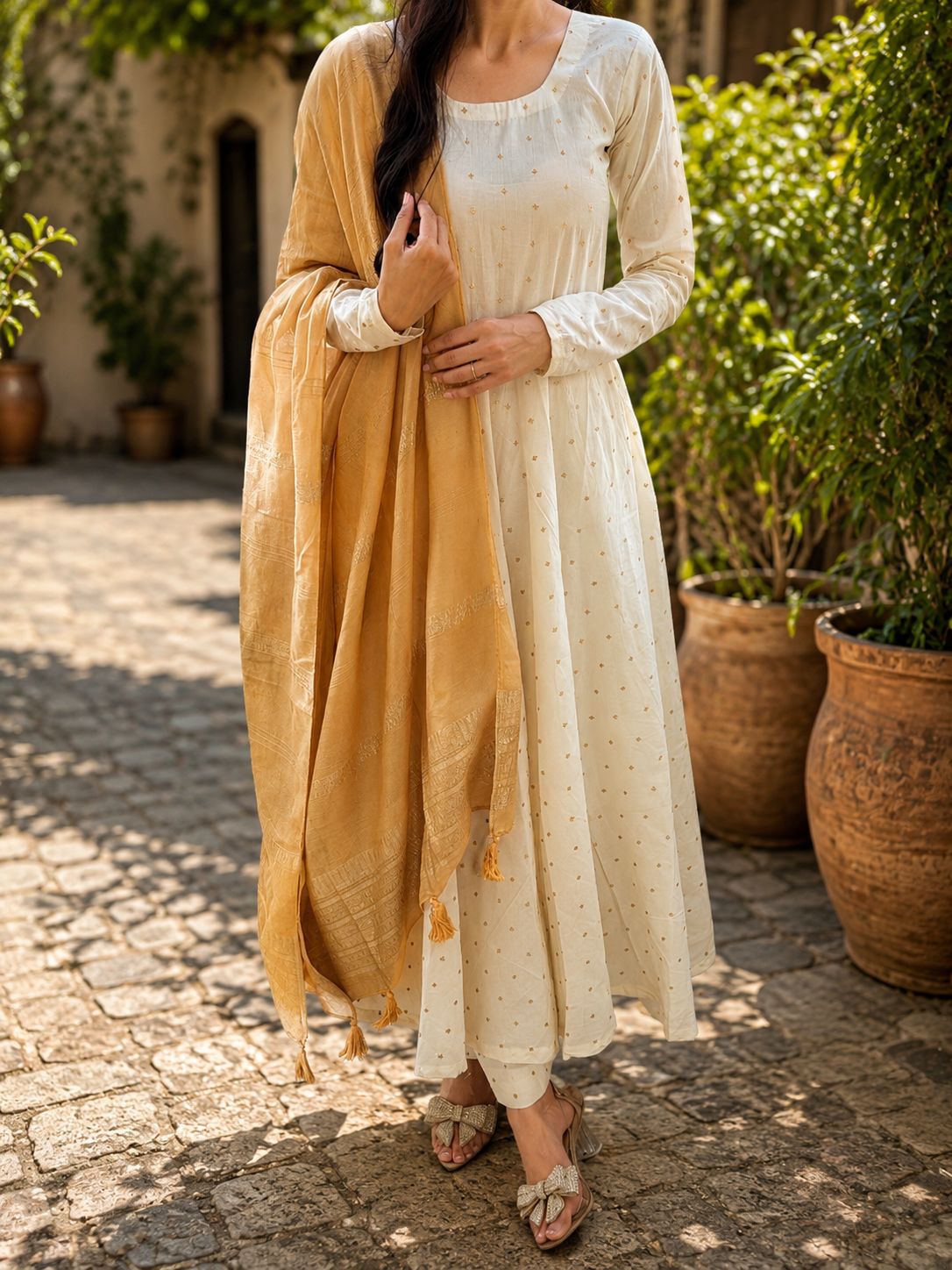 Woman in a cream-colored traditional outfit with a yellow dupatta standing outdoors.