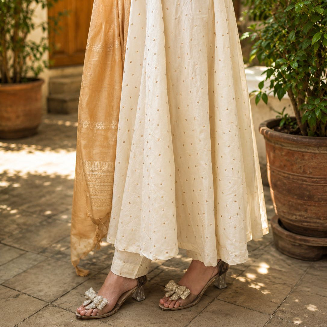 Person wearing a long, light-colored dress with a patterned skirt in an outdoor setting.