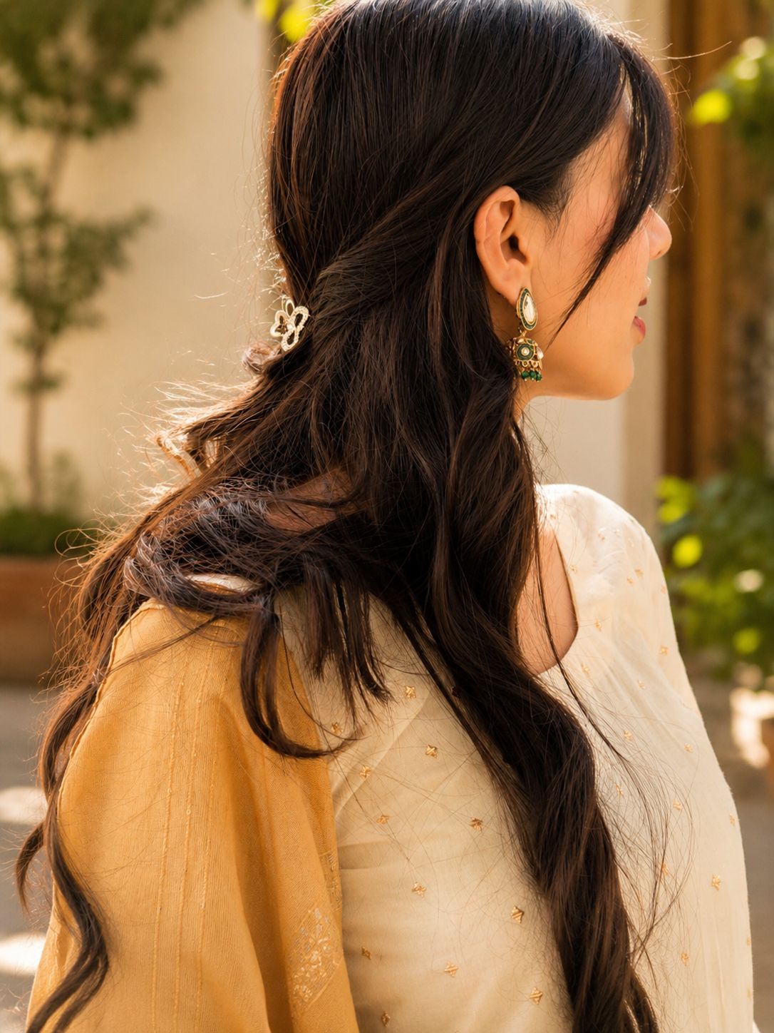Woman with long dark hair styled in a braid, wearing earrings, in an outdoor setting.